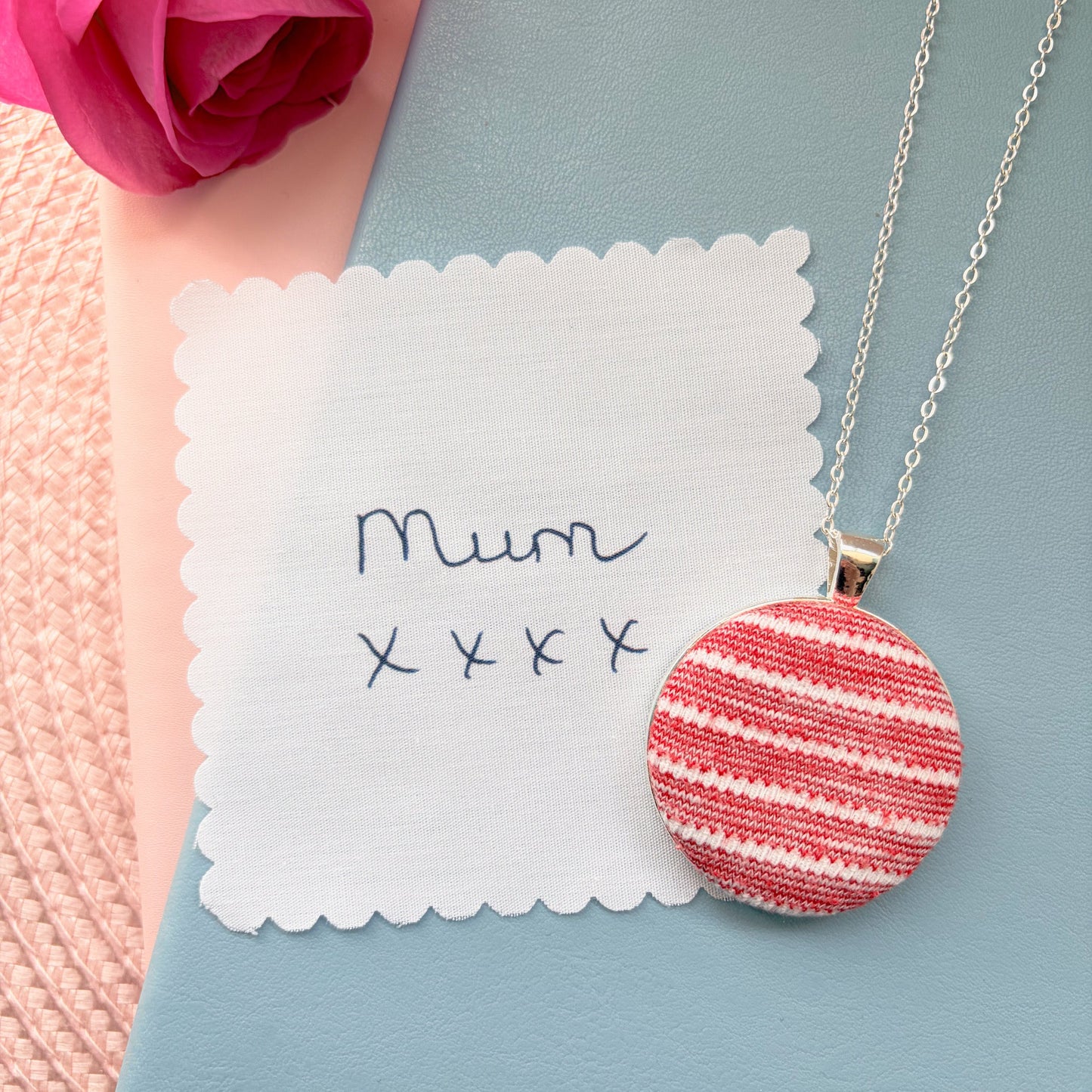 Necklace with a red and white striped pendant with 'Mum' and 'xxx' on a blue surface.