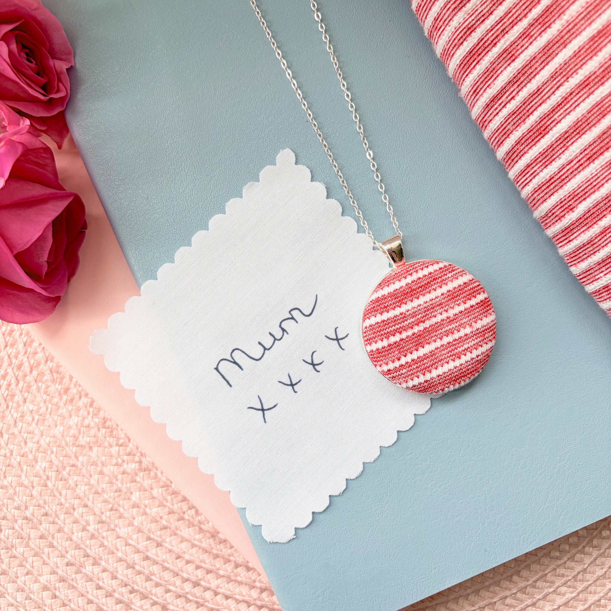 Necklace with a red and white striped pendant with 'Mum x x x' text, surrounded by pink flowers and fabric.