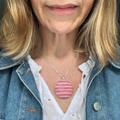 Person wearing a red striped fabric pendant and a denim jacket and white blouse