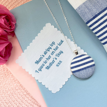 Necklace with a blue and white striped pendant with fabric message on a blue notebook with pink roses.