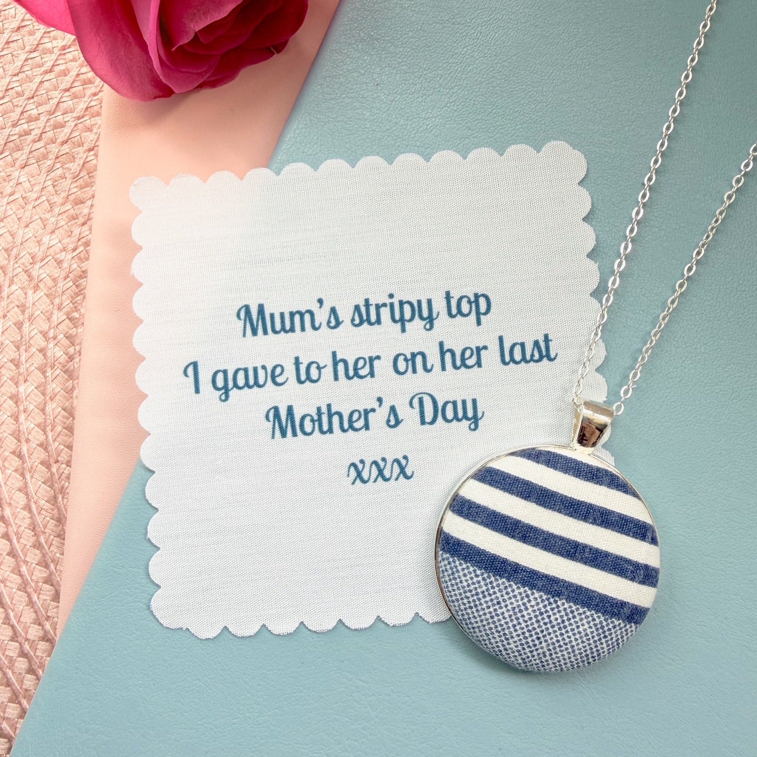 Necklace with a blue and white striped pendant with fabric message, placed on a blue notebook.
