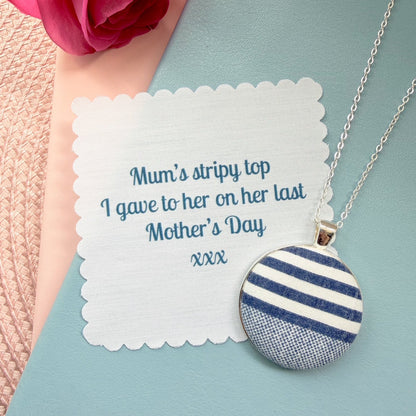 Necklace with a blue and white striped pendant with fabric message, placed on a blue notebook.