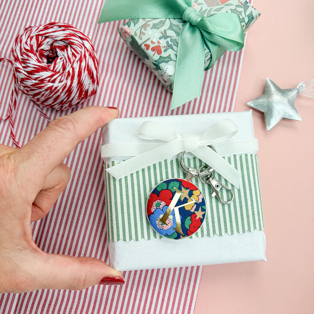 Personalised Christmas Gift Tag and Keyring, made with blue Liberty floral and star fabric, printed with K in gold, set in a keyring, thread on a white velvet ribbon, tied around a small gift and set on a Christmas flatlay