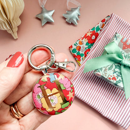 Personalsied gift tag which doubles up as a keyring, made with Liberty of London red floral and star fabric, with an H in gold print, on a Christmas flatlay
