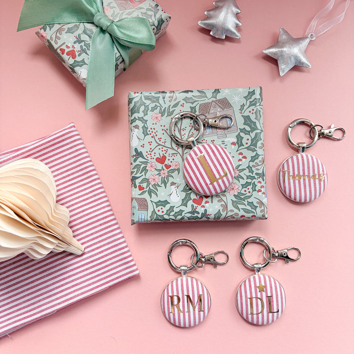 Personalised Christmas Gift Tags and Keyrings, made with festive red striped fabric, printed with names and initials in gold foil, set in a keyring and set on a Christmas flatlay
