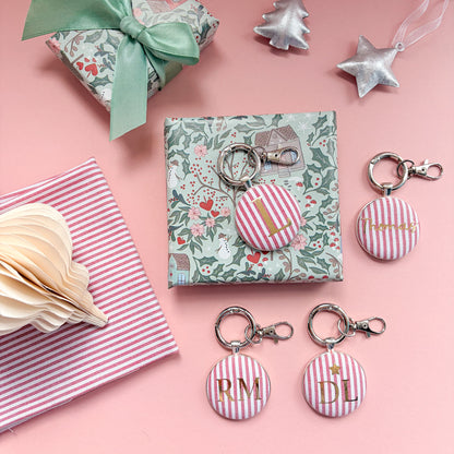 Personalised Christmas Gift Tags and Keyrings, made with festive red striped fabric, printed with names and initials in gold foil, set in a keyring and set on a Christmas flatlay
