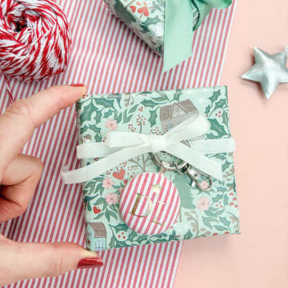 Personalised Christmas Gift Tag and Keyring, made with festive red striped fabric, printed with initials DL and a small star in gold foil, set in a keyring, thread on a white velvet ribbon, tied around a small gift and set on a Christmas flatlay