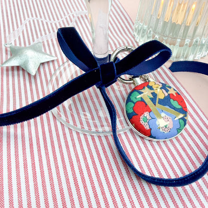 Personalised Initial Keyring used as a place setting, made with blue Liberty floral fabric, with a gold K initial, thread on a blue velvet ribbon, tied around a wine glass