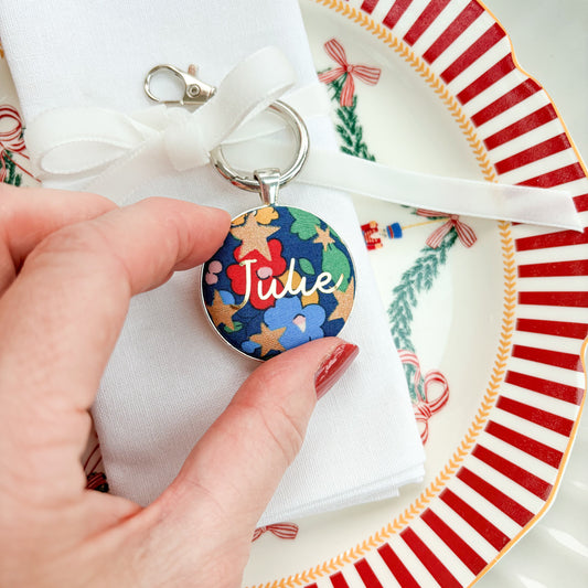 Personalised keyring tied on a velvet ribbon, around a serviette as a place setting, made with blue Liberty floral fabric, printed with Julie in gold 