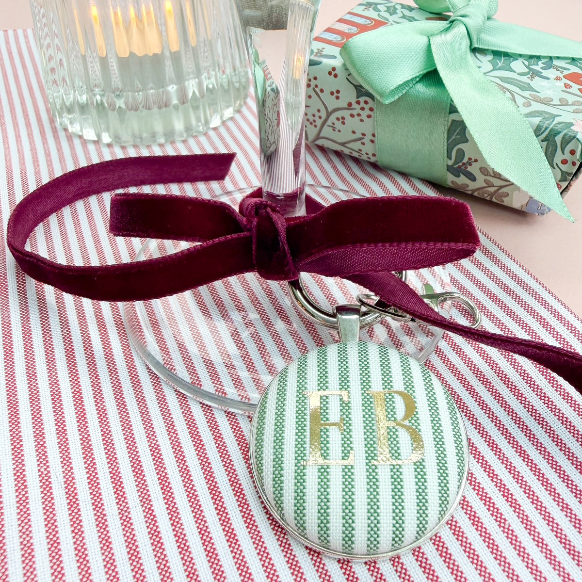 Personalised name place setting for the Christmas table, made with green striped fabric, printed with Katie in gold, set in a silver plated keyring, thread on a burgundy velvet ribbon, tied around a wine glass