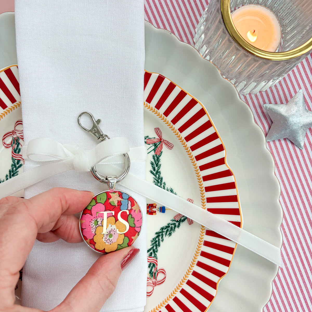 Personalised table place setting, designed as a keyring, with red Liberty floral fabric, gold initials, thread on a velvet ribbon and tied around a napkin, on Christmas plates