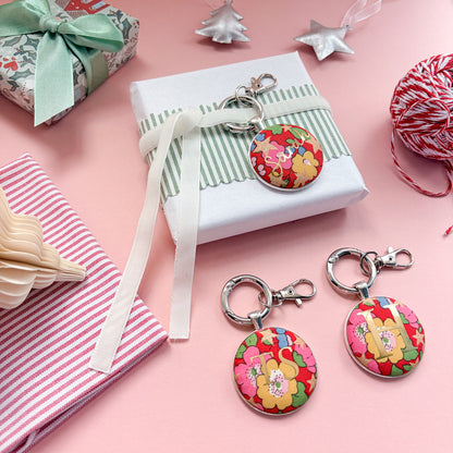 Personalised gifts tags set in keyrings, made with red floral Liberty fabrics, printed with gold names and initials, on a Christmas flat lay