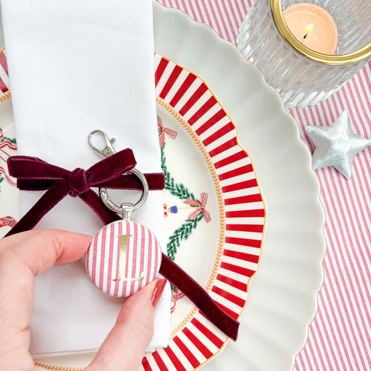 Red striped Christmas place setting, with gold initial, set in a silver plated keyring, thread on burgundy velvet ribbon, around a napkin on Christmas plates