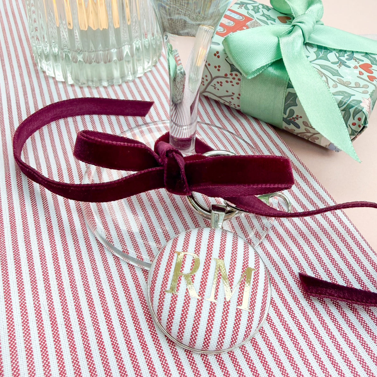 Personalised initial keyring used as a place setting, made with red striped fabric, printed with gold initials, thread on a burgundy velvet ribbon, tied around a wine glass