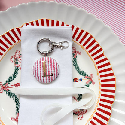 Initial Christmas table place setting, made with red striped fabric, printed with a gold L initial, set in a keyring, displayed on a white napkin and Christmas plates