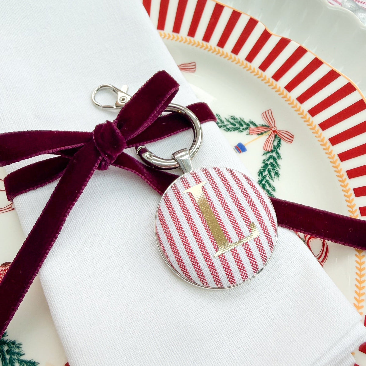 Red striped Christmas table place setting personalised with a gold L, made with red striped fabric, thread on a velvet ribbon around  white napkin