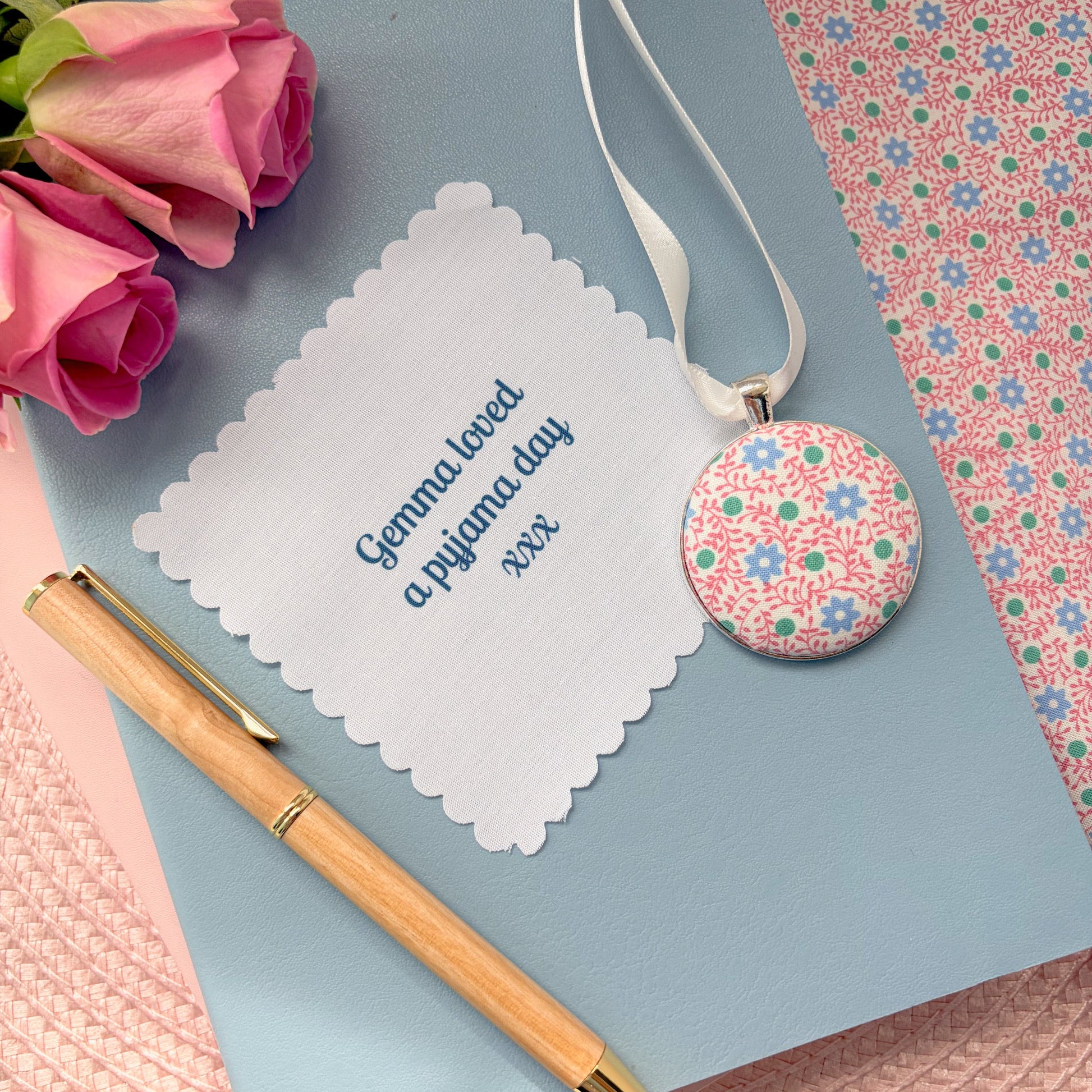Floral pyjamas memory keepsake, thread on a ribbon, with a fabric message, set on a blue notebook with a pen and rose