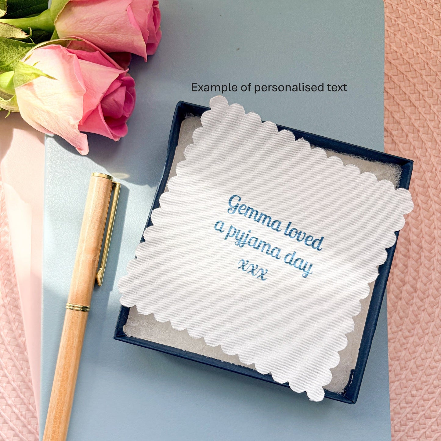 Floral pyjamas memory keepsake, thread on a ribbon, with a fabric message, set on a blue notebook with a pen and rose