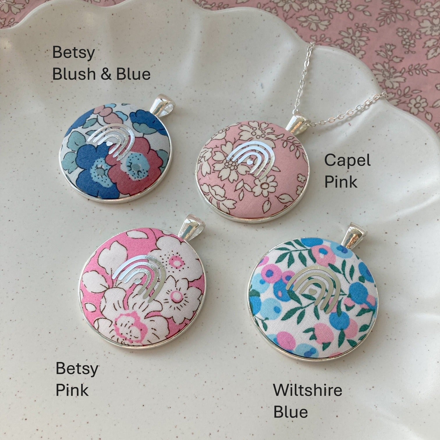Four floral pendant necklaces on a decorative plate with labels indicating names and colors.