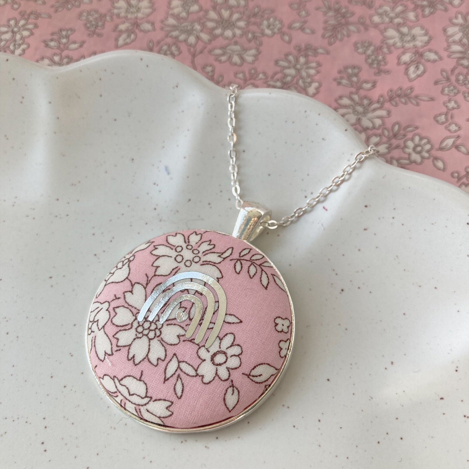 Silver rainbow necklace on pink floral fabric