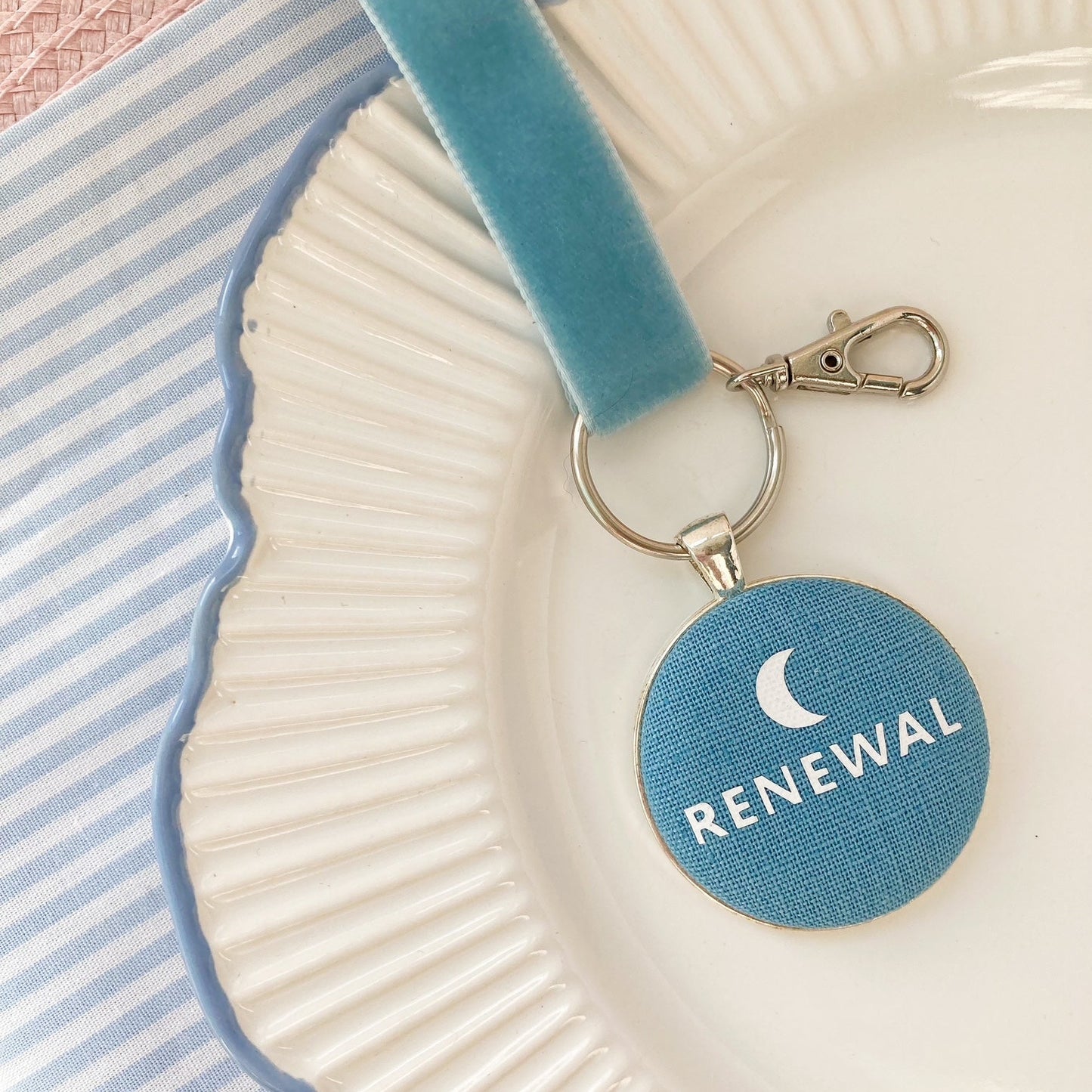 Blue keychain with 'Renewal' and a new moon printed onto fabric