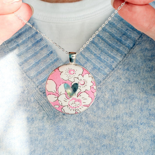 Secret Mantra necklace with a silver heart printed on a Liberty pink floral fabric, thread on a silver chain and worn with a pale blue jumper