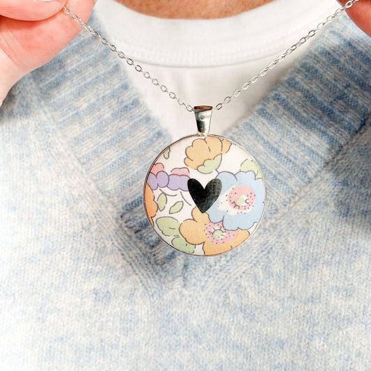 Secret Mantra necklace with a silver heart printed on a Liberty yellow & lilac floral fabric, thread on a silver chain and worn with a pale blue jumper