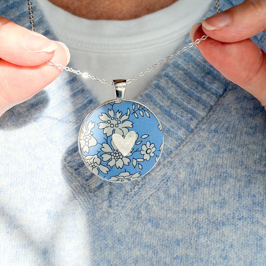 Secret Mantra necklace with a silver heart printed on a Liberty blue floral fabric, thread on a silver chain and worn with a pale blue jumper