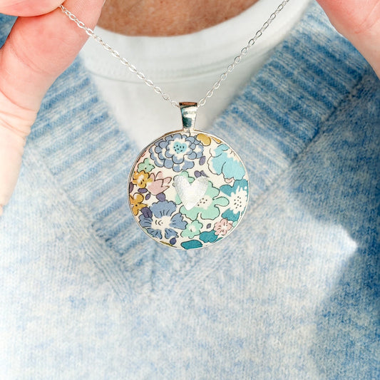 Secret Mantra necklace with a silver heart printed on a Liberty teal floral fabric, thread on a silver chain and worn with a pale blue jumper