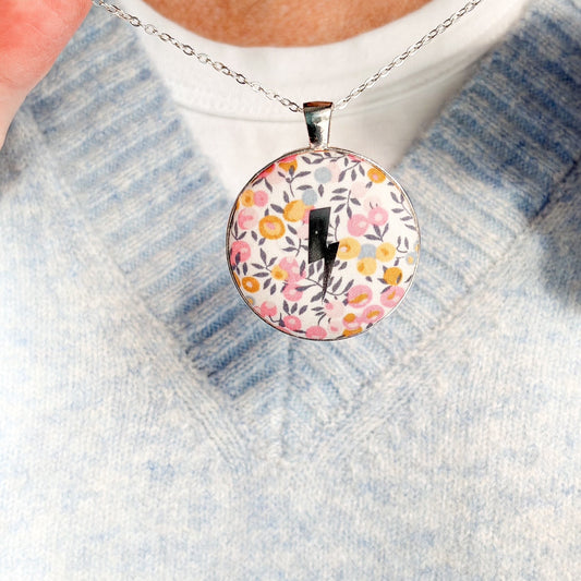 Secret Mantra necklace with a silver lightning printed on a Liberty yellow & pink floral fabric, thread on a silver chain and worn with a pale blue jumper