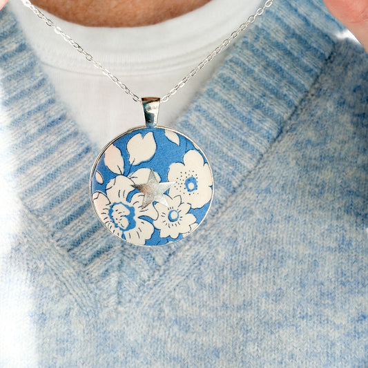 Secret Mantra necklace with a silver star printed on a Liberty blue floral fabric, thread on a silver chain and worn with a pale blue jumper
