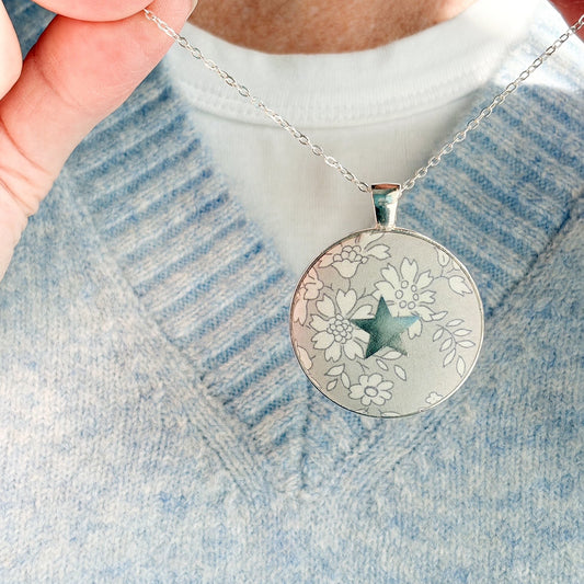 Secret Mantra necklace with a silver star printed on a grey Liberty floral necklace, thread on a silver chain and worn with a pale blue jumper