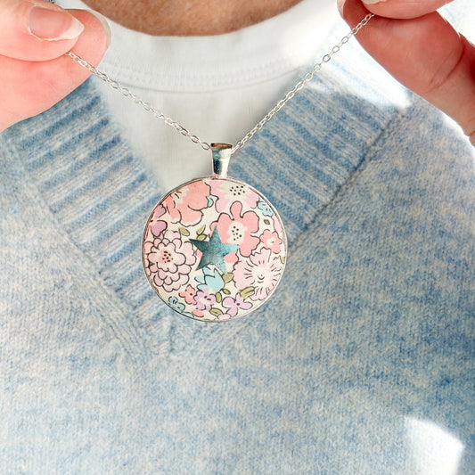 Secret Mantra necklace with a silver star printed on a pink Liberty floral fabric, thread on a silver chain and worn with a pale blue jumper