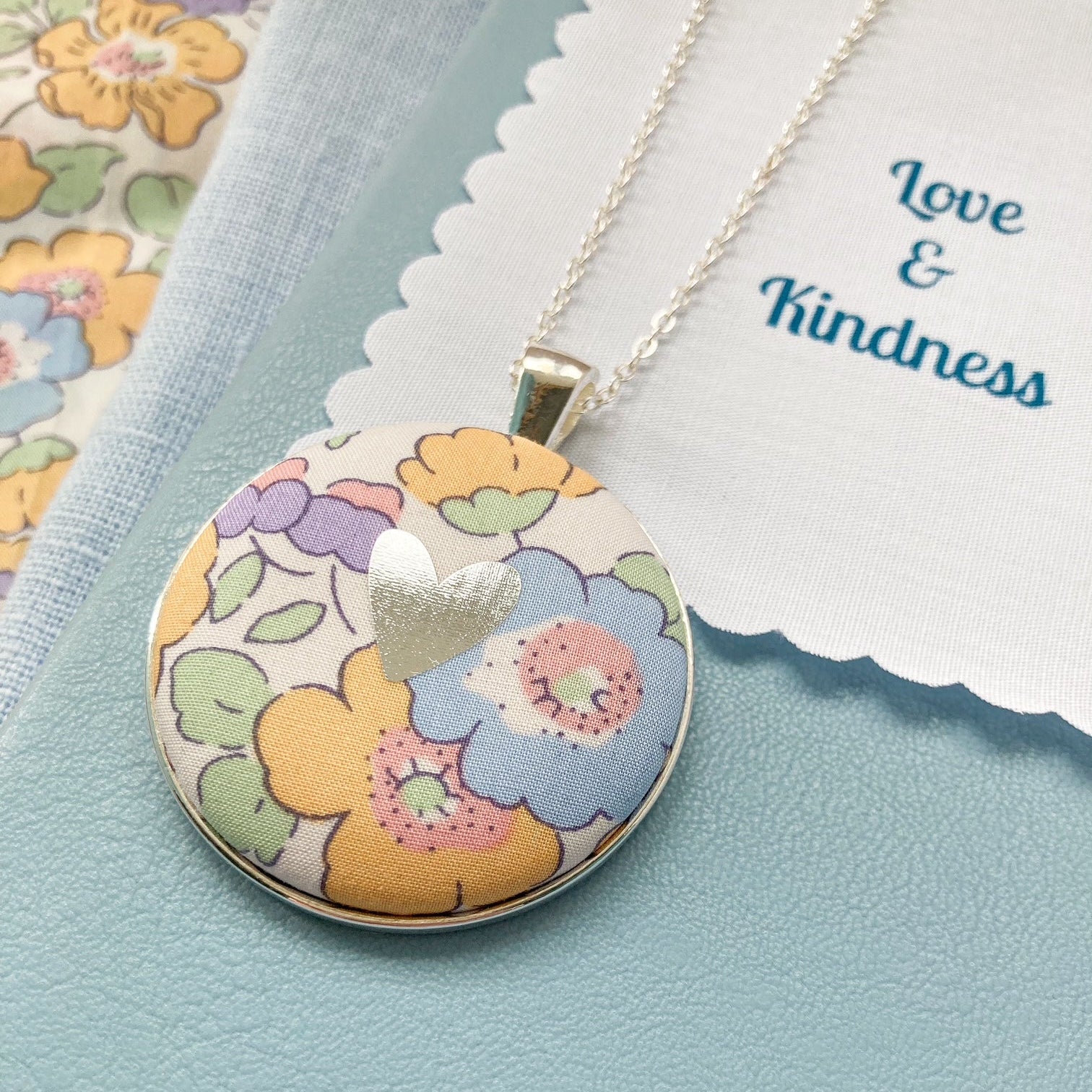 Yellow & lilac floral necklace with a silver foil heart on a blue book