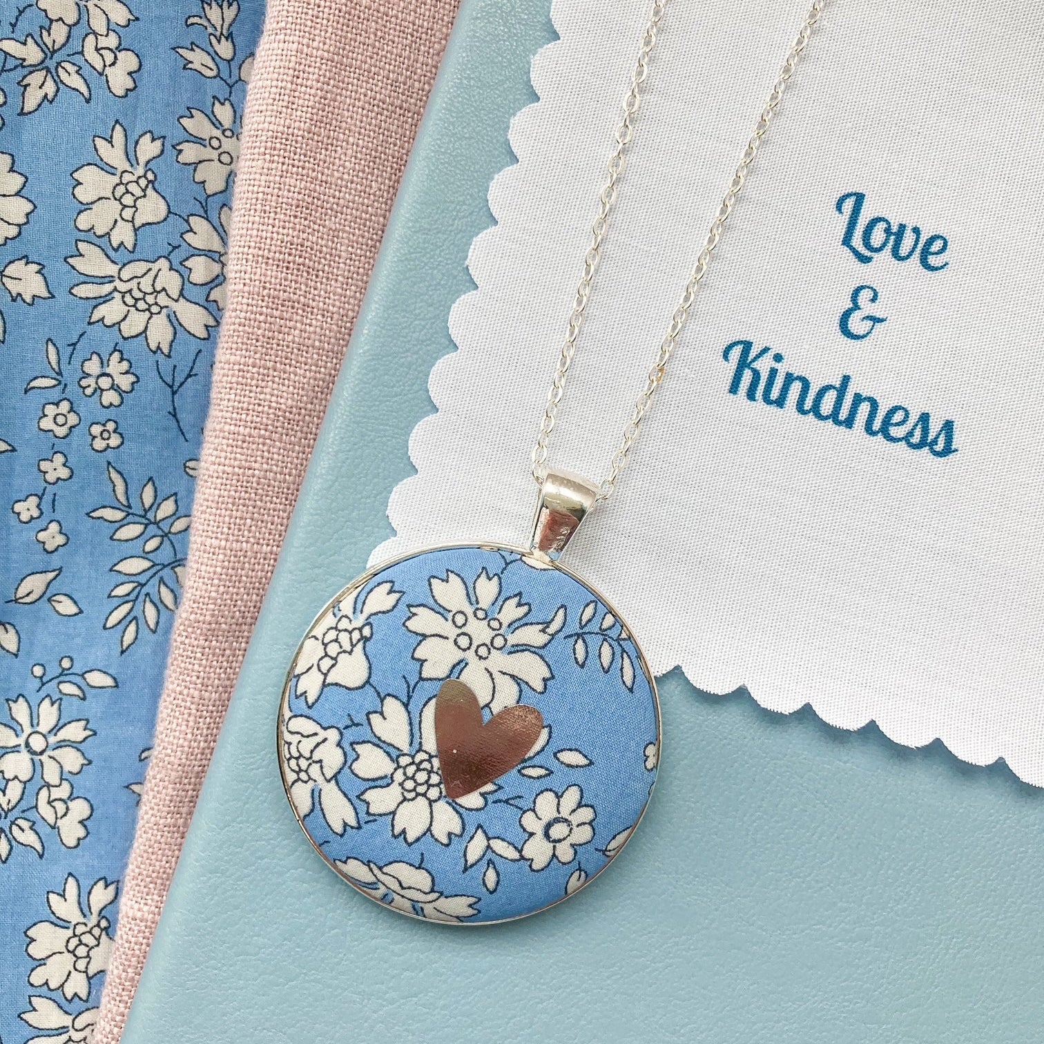 Blue floral necklace with a silver foil heart and a fabric message saying "Love & Kindness"