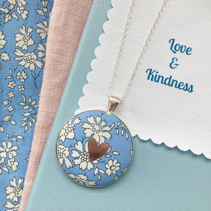 Blue floral necklace with a silver foil heart and a fabric message saying "Love & Kindness"