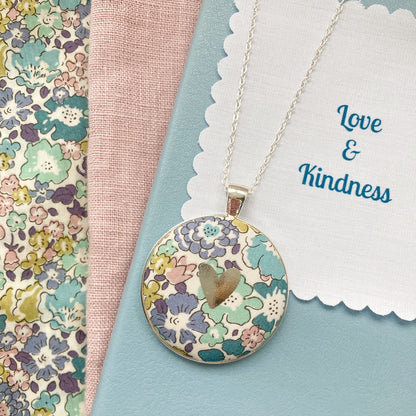 Teal & purple floral necklace with a silver heart and a fabric message saying "Love & Kindness"