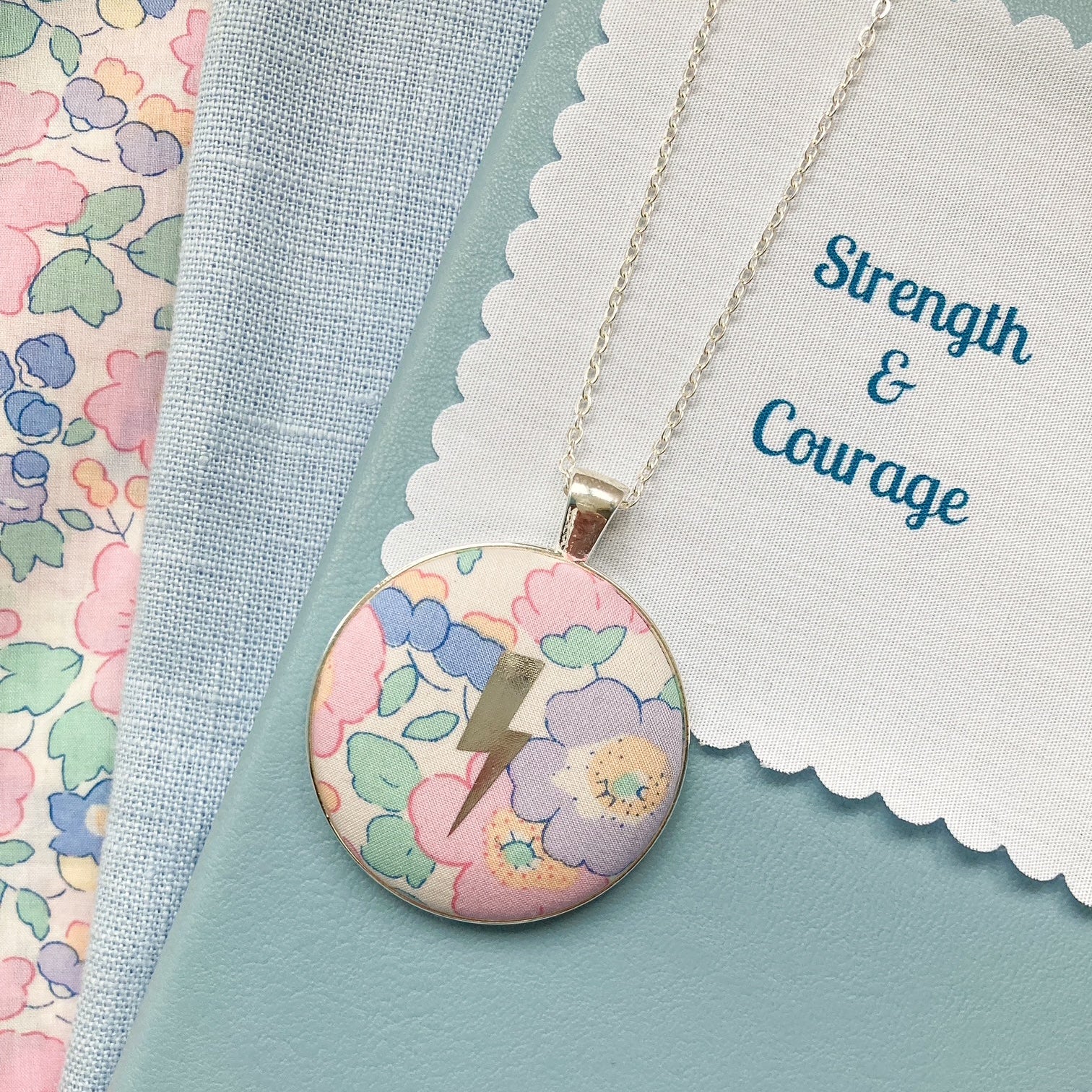 Pastel floral Liberty necklace with a lightning design and a fabric message saying Strength & Courage