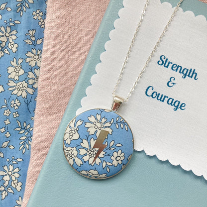Blue liberty floral fabric necklace with a silver lightning design and a fabric message saying "Strength & Courage"