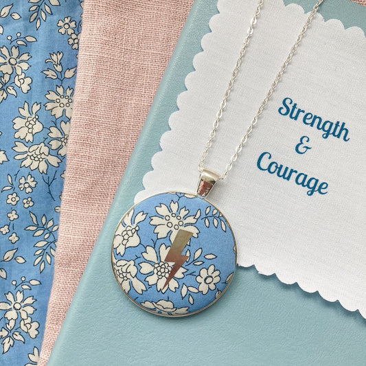 Blue liberty floral fabric necklace with a silver lightning design and a fabric message saying "Strength & Courage"