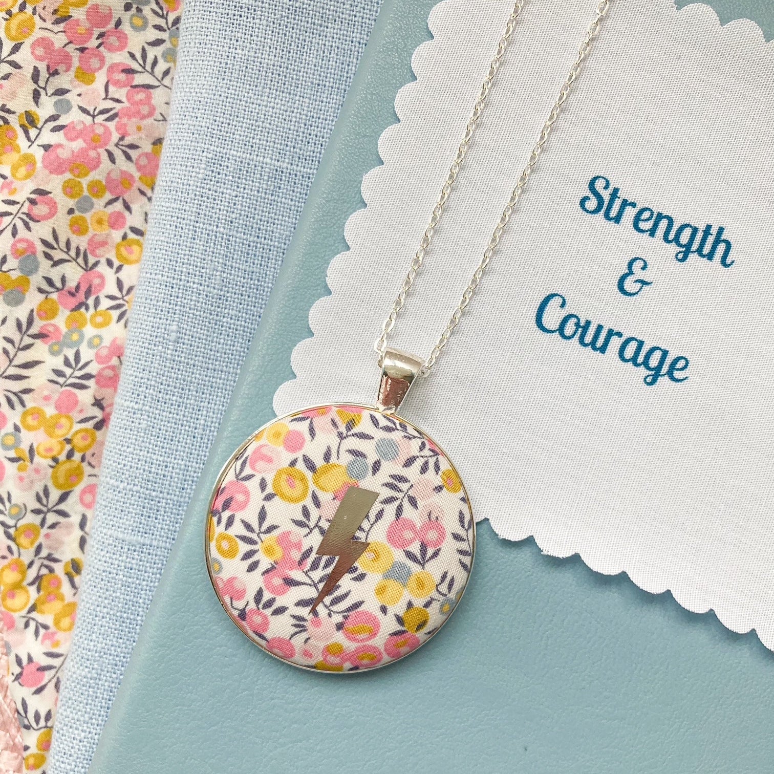Liberty of London fabric necklace with a lightning design with a fabric message saying "Strength & Courage"