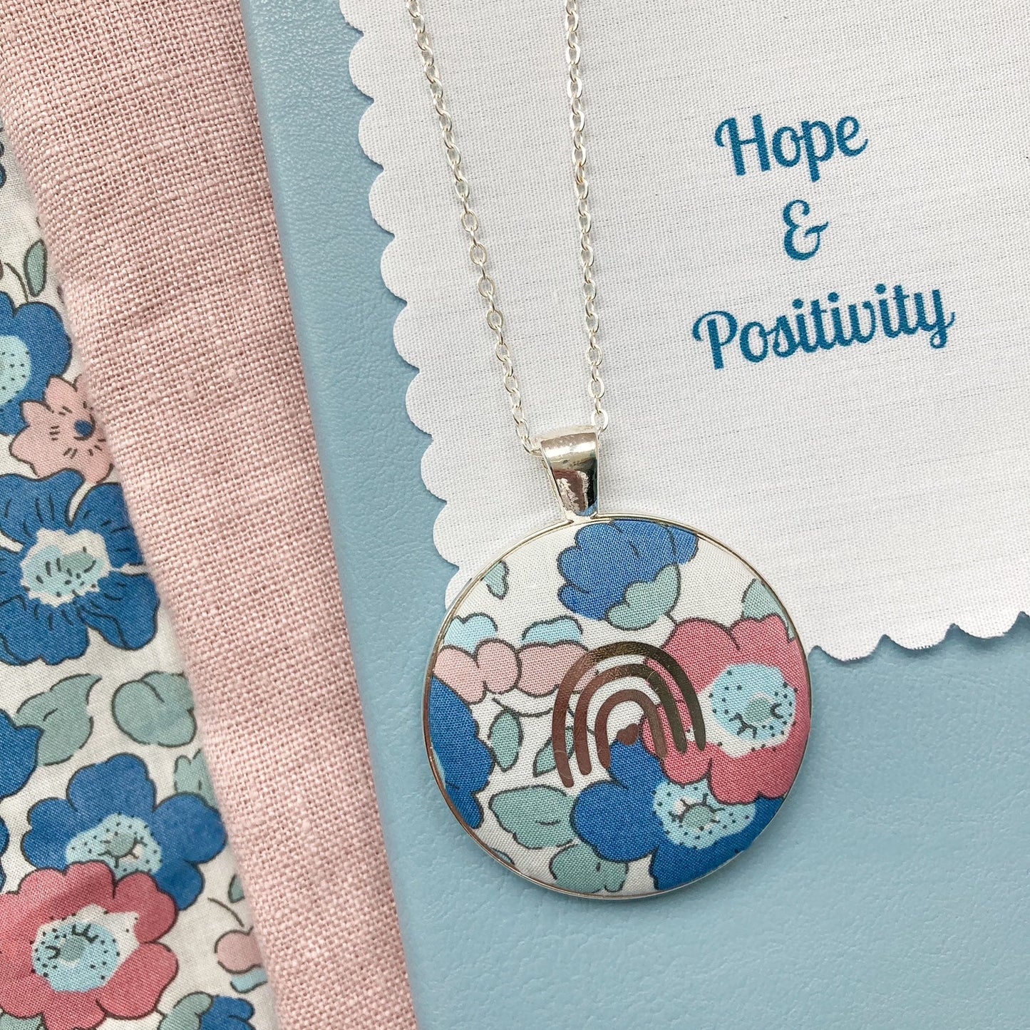 Necklace with floral pendant and rainbow design with a fabric message printed 'Hope & Positivity'