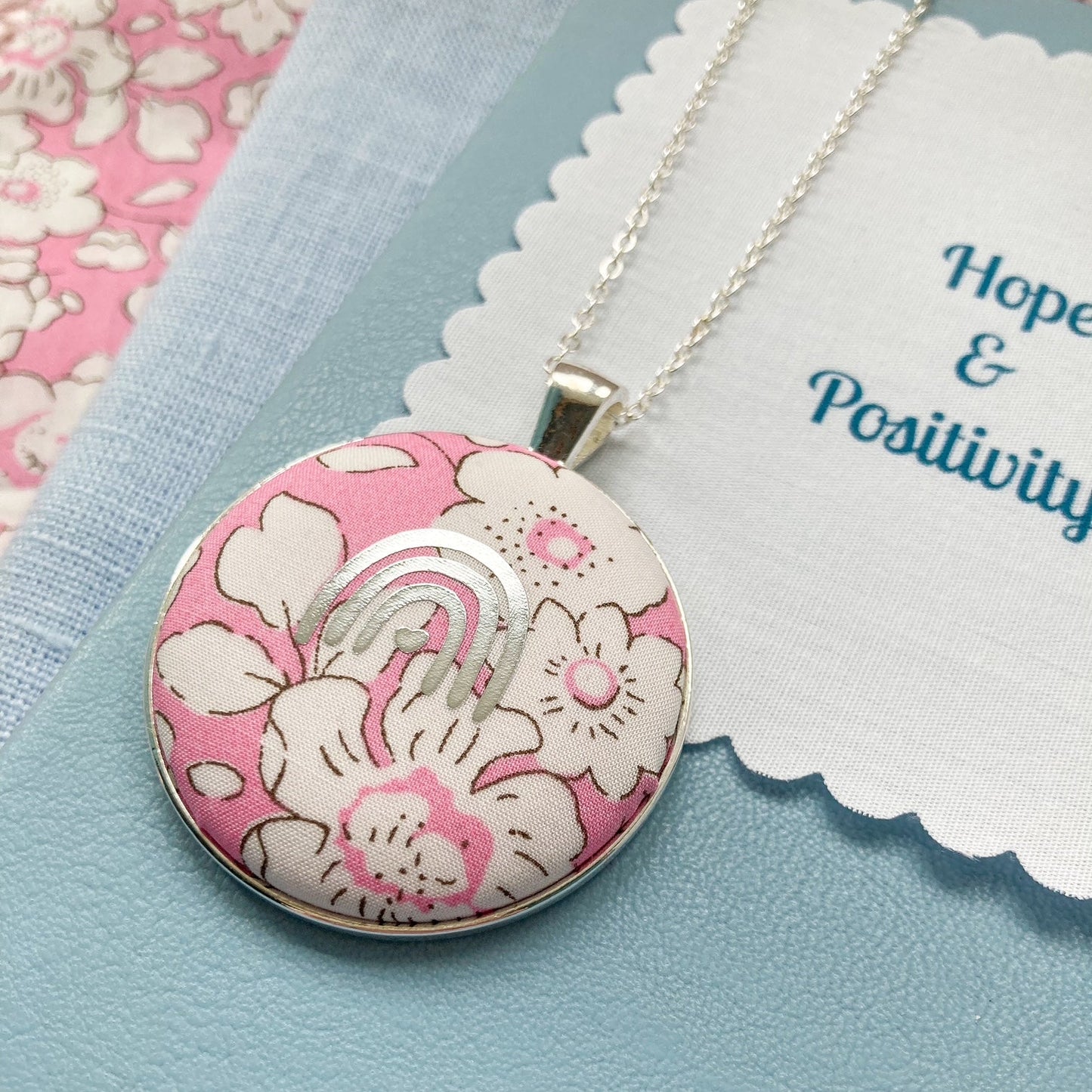 Pink rainbow necklace with a floral pendant on a blue background
