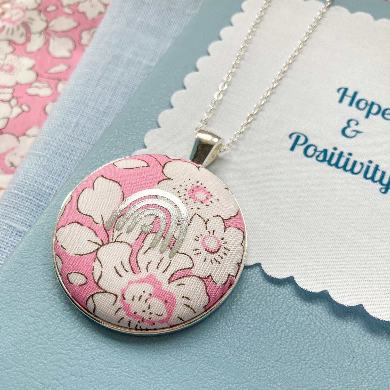 Pink rainbow necklace with a floral pendant on a blue background