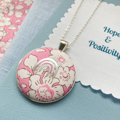 Pink rainbow necklace with a floral pendant on a blue background