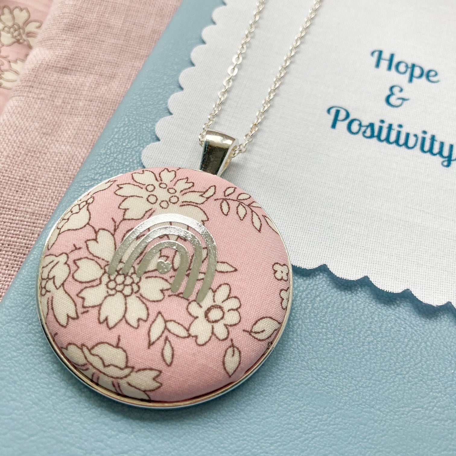 Necklace with a pink floral pendant and a fabric message with 'Hope & Positivity' text.