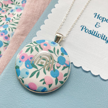 Floral pendant necklace on a blue background with a fabric message that says 'Hope & Positivity'.