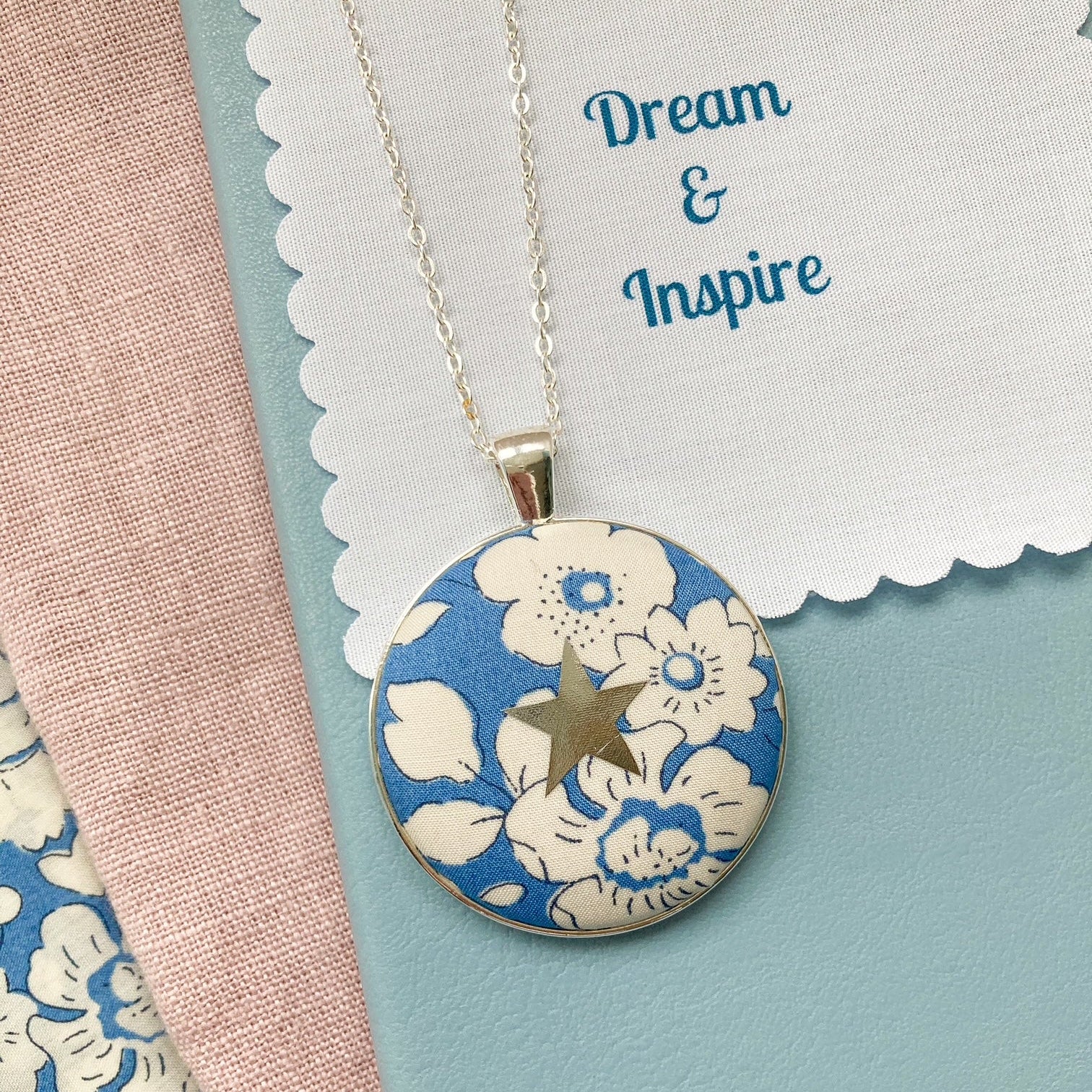 Blue floral necklace with a silver star and a fabric message saying "Dream & Inspire"