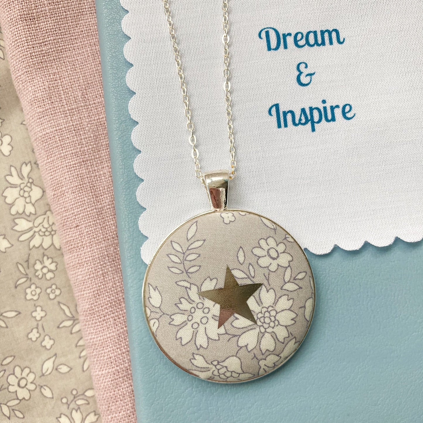 Grey floral necklace with a star design and a fabric message saying "Dream & Inspire"