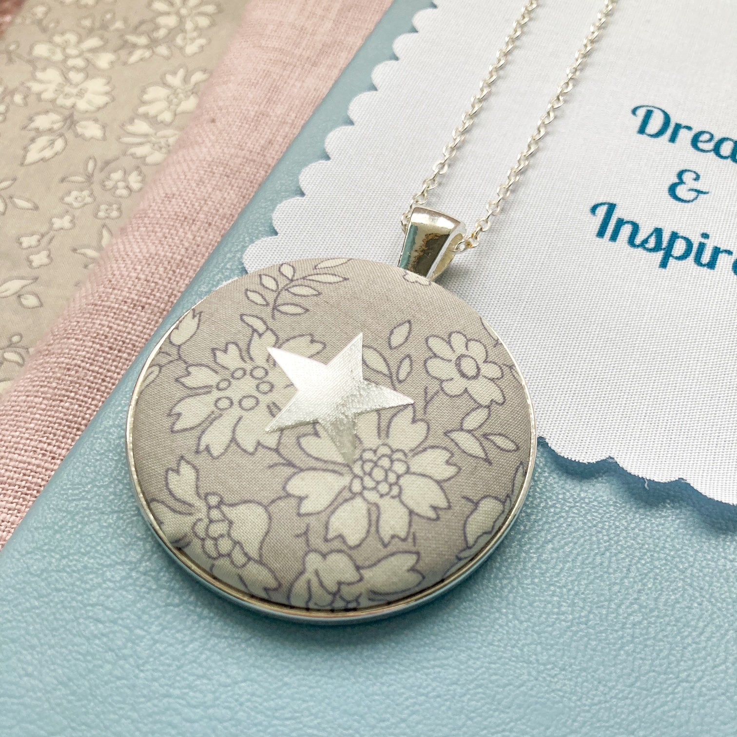Grey Liberty floral necklace with a star design on a blue book